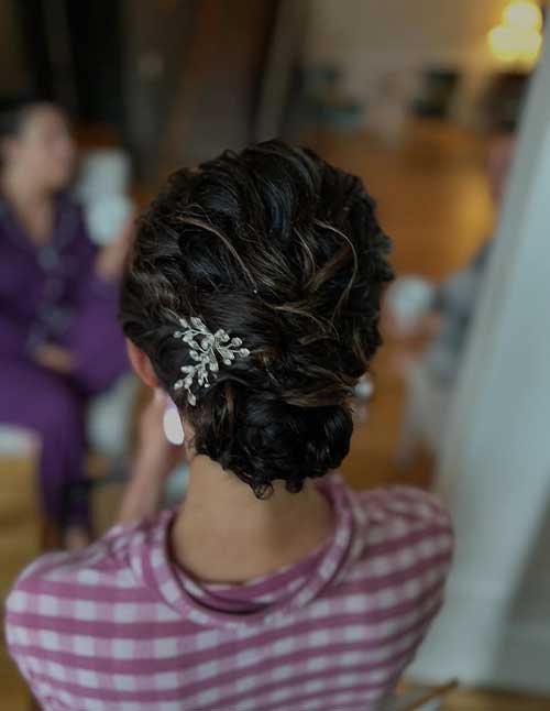 Back view of a curly twisted updo pinned low at the nape, finished with a sparkly floral hair clip.