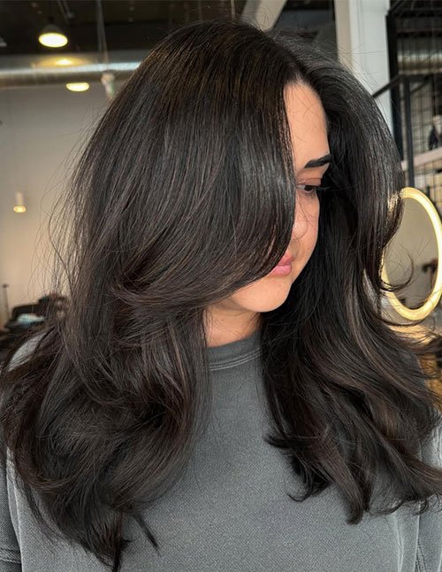 Front view of a woman wearing a winter soft blowout look with long, glossy layers and bouncy, face-framing volume.